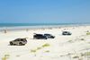 Cars parked by a wide sandy beach.