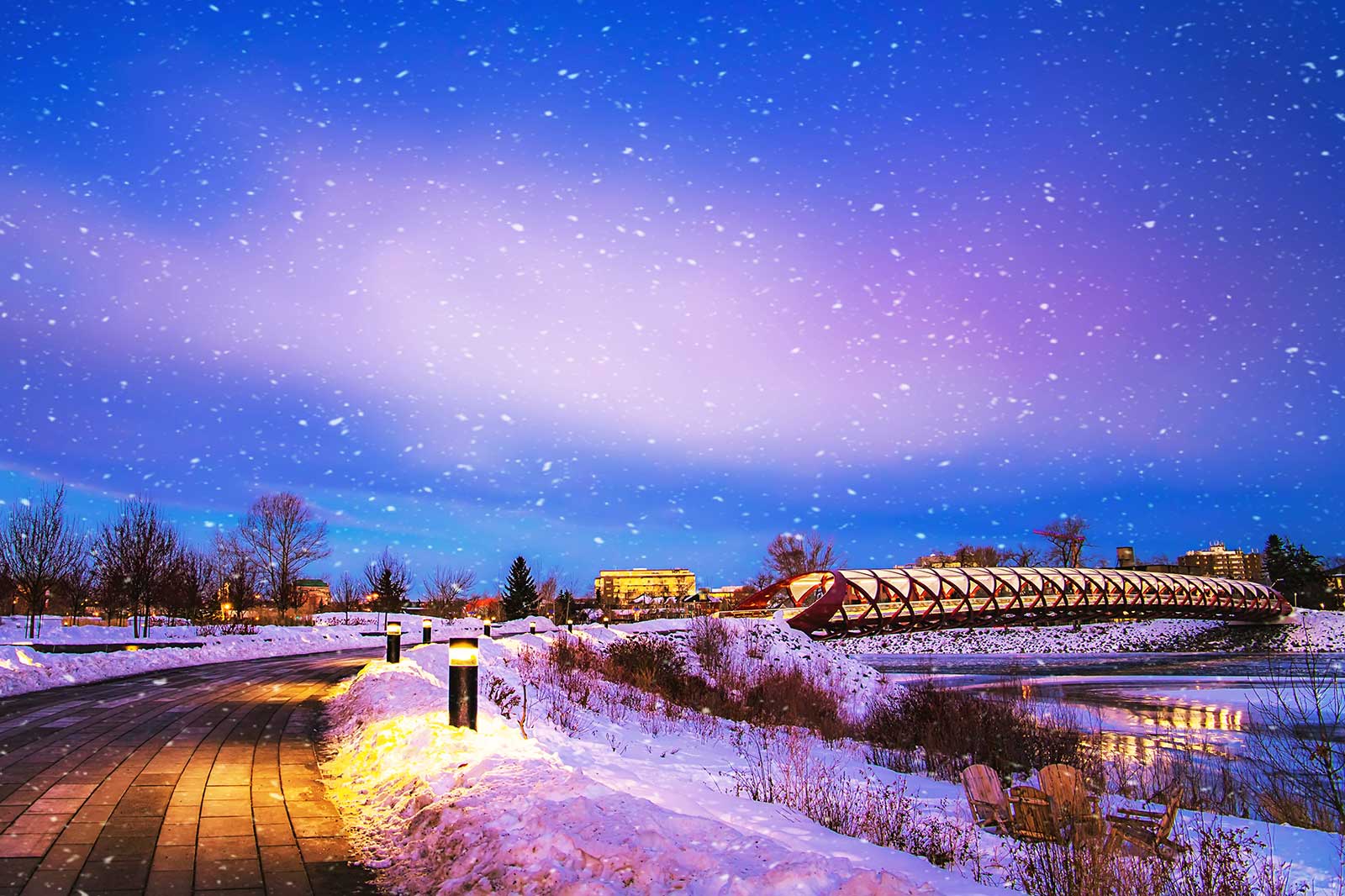 Snowfall at night, a lit bridge in the background.