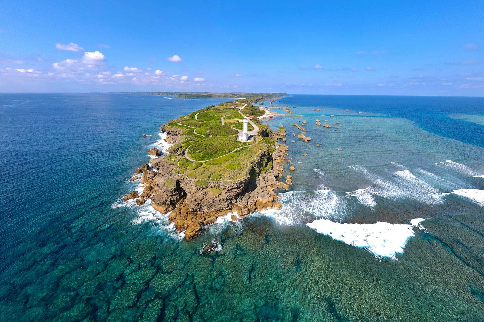 A green cape with vegetation and white lighthouse.