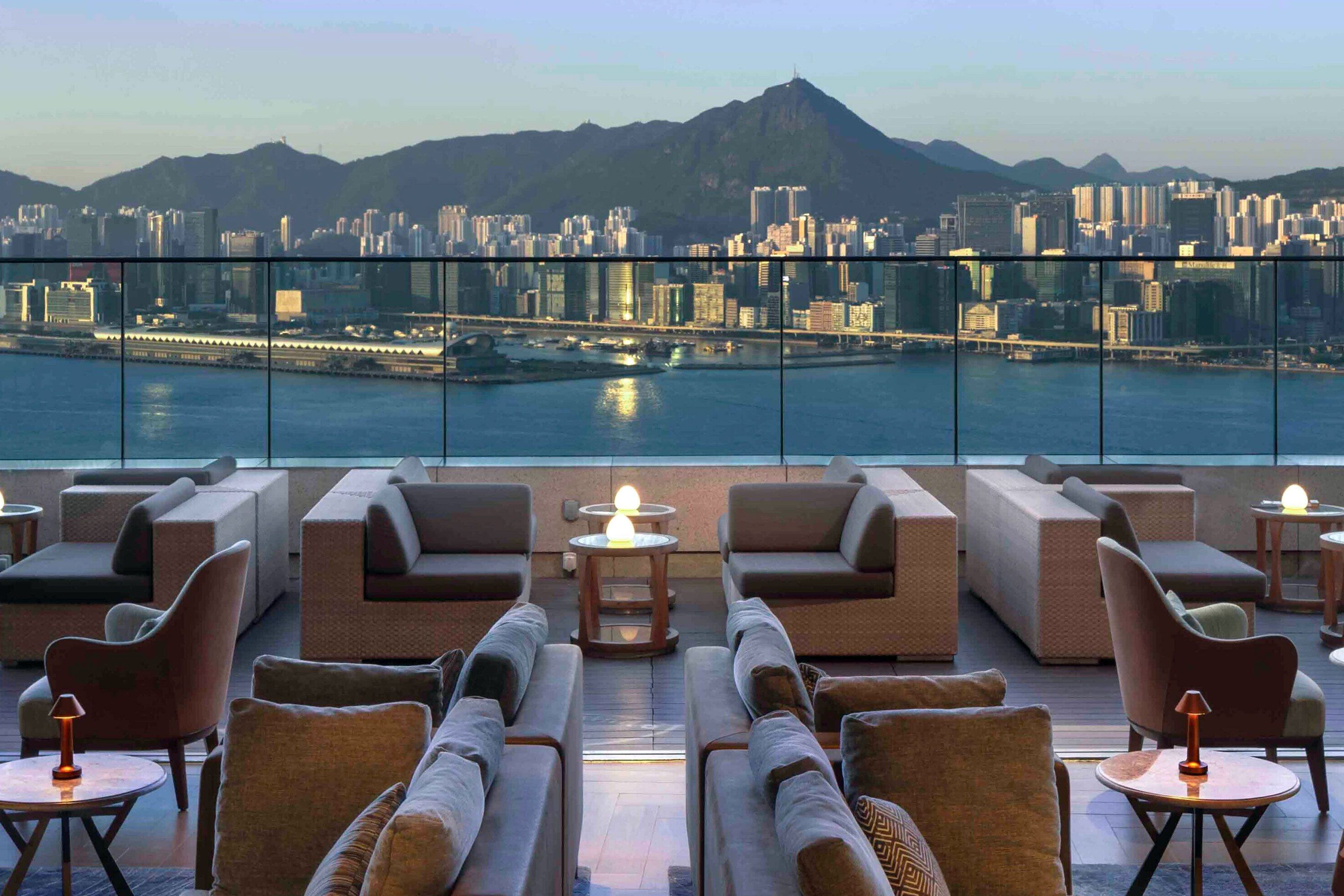 Seating and tables at dusk on a rooftop bar with a skyline view.