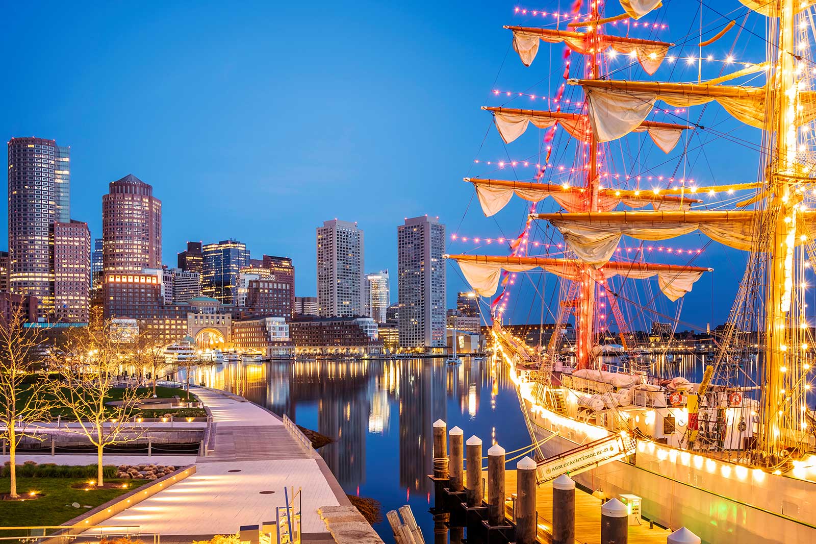 Skyline of a city at night with ship decorated with lights in the foreground.
