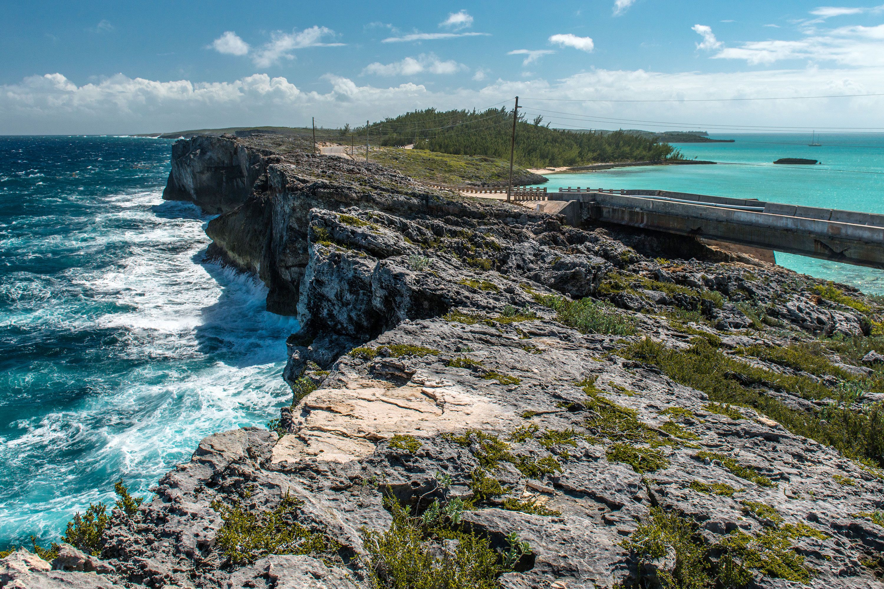 Waves crash on a large rock wall on one side with clear turquoise blue water on the other side in the Bahamas.