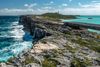 Waves crash on a large rock wall on one side with clear turquoise blue water on the other side in the Bahamas.
