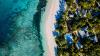 An aerial view of crystal-clear waters crashing onto a beach and houses among palm trees in Fiji.