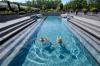 Two people swim in an outdoor pool at a spa on a sunny day.