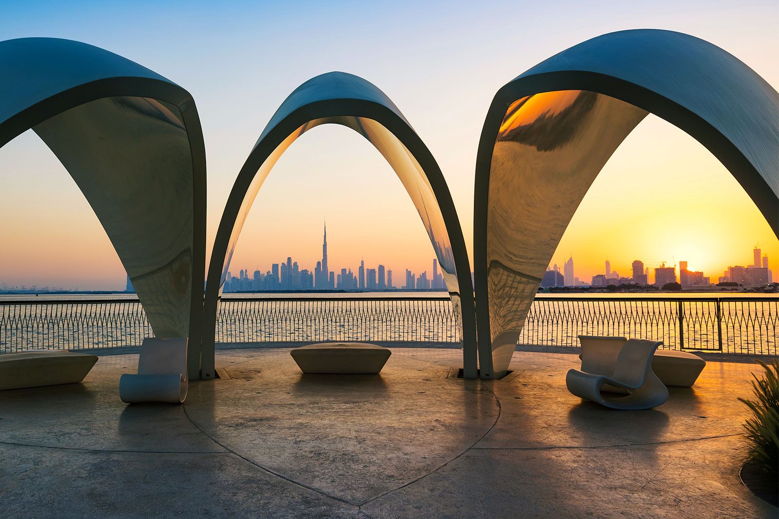 A beautiful view of Dubai city skyline through sculptures in the evening with a colorful sky.