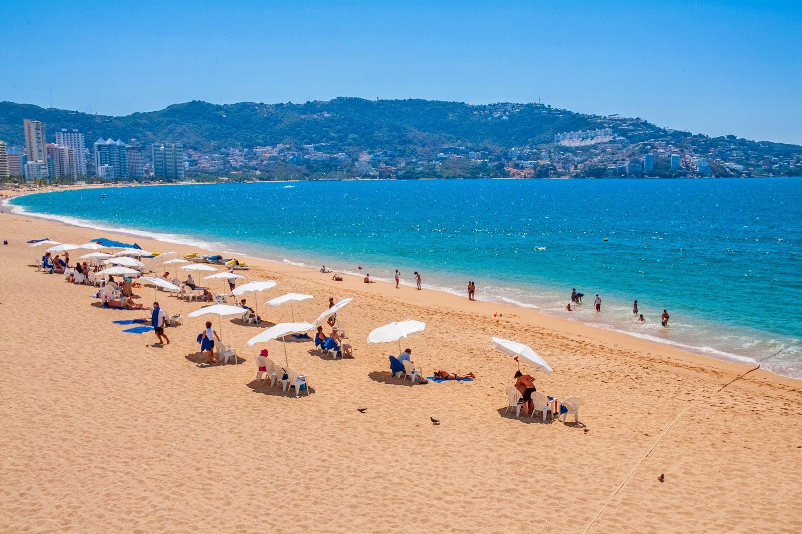 People under beach umbrellas along a sandy ocean beach.