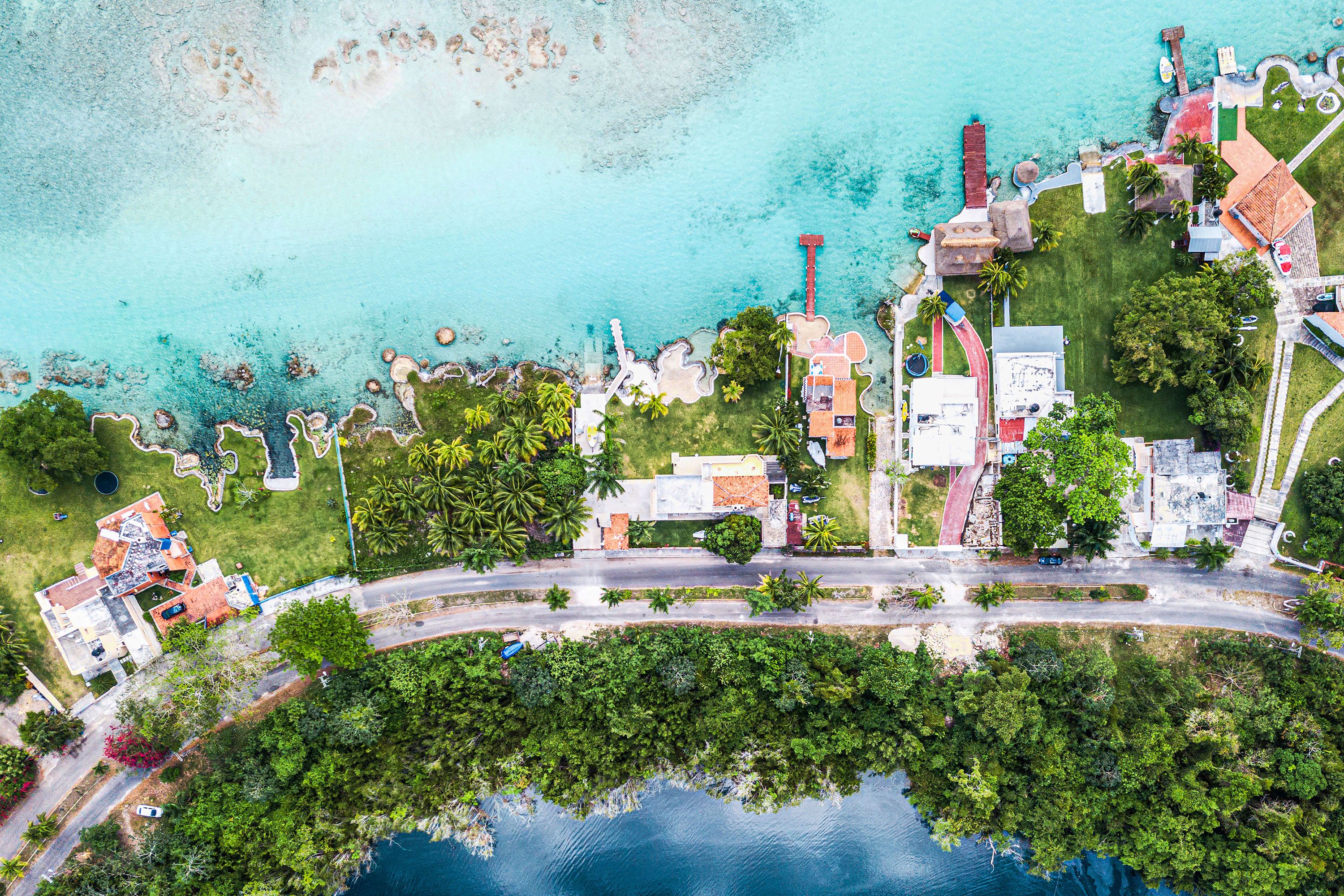 Direct overhead view of a vegetation rich stretch of land with large homes surrounded by the sea a a lagoon.
