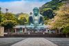 Statue of Buddha on a large square, trees in the background.