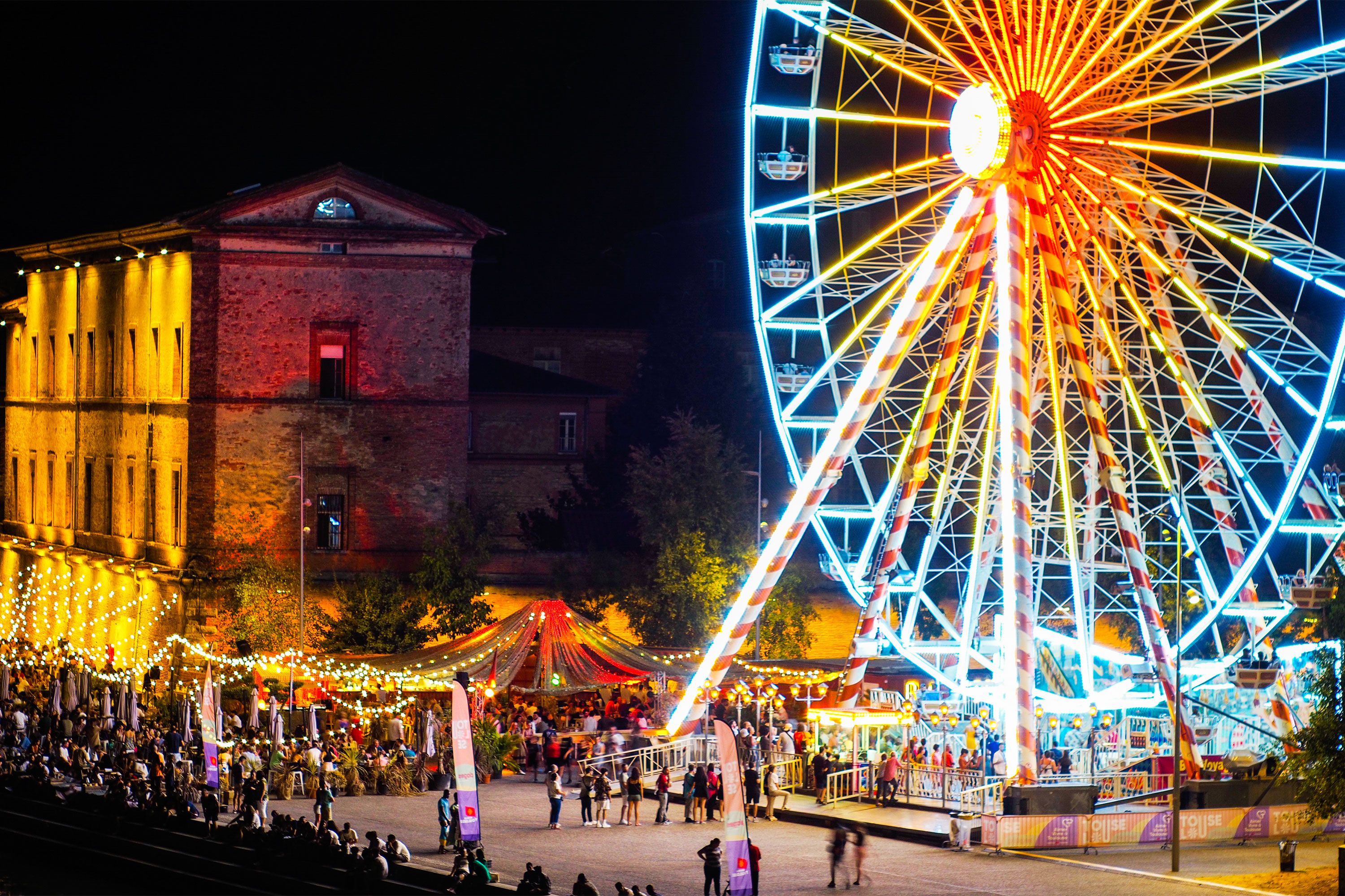 A ferris wheel is lit up at night during a festival.