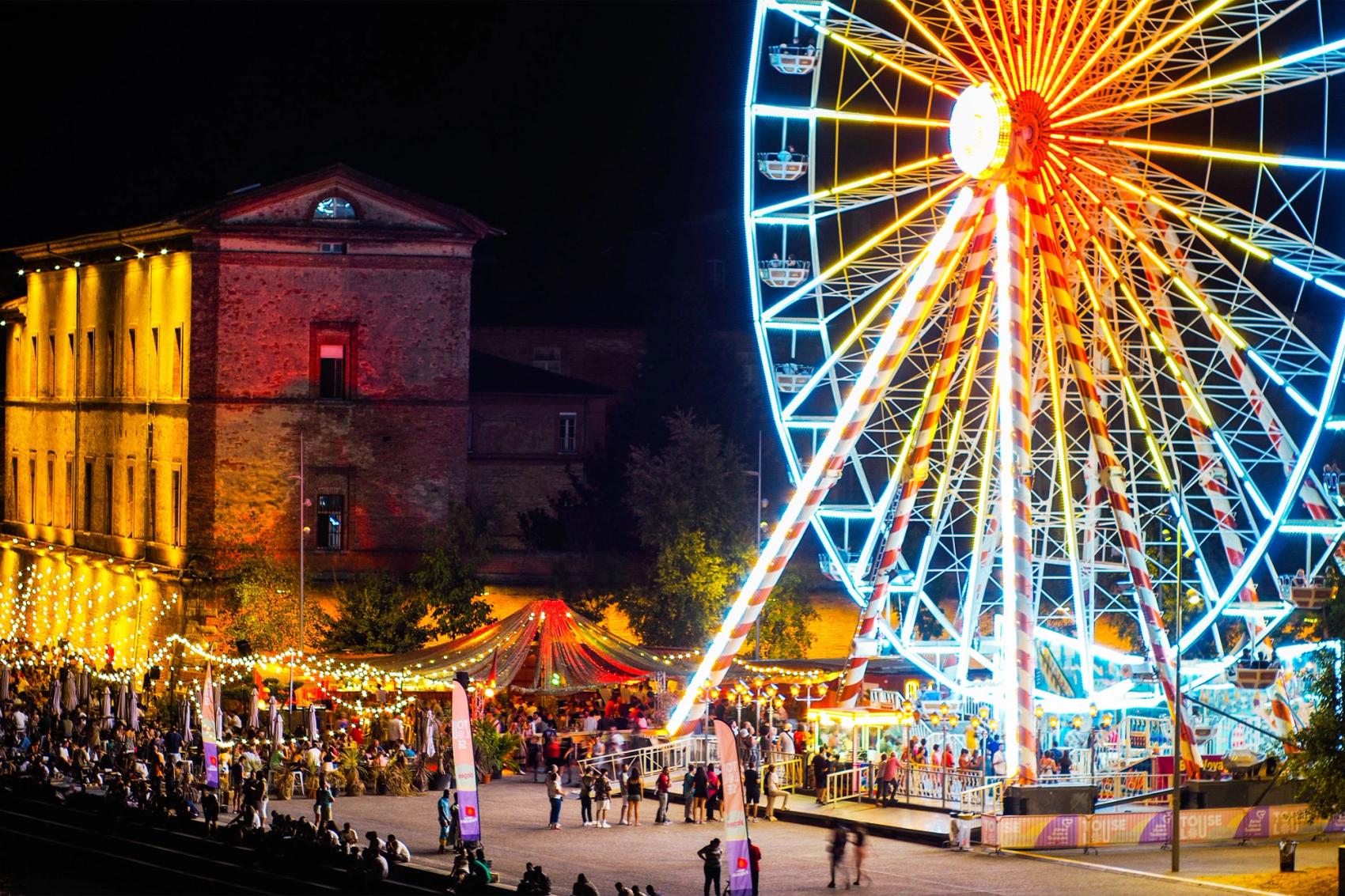 A ferris wheel is lit up at night during a festival.