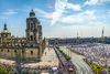 Panoramic view looking down into a large crowded square with church and jets flying overhead.