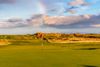 A flag on a golf course with clouds and a rainbow.