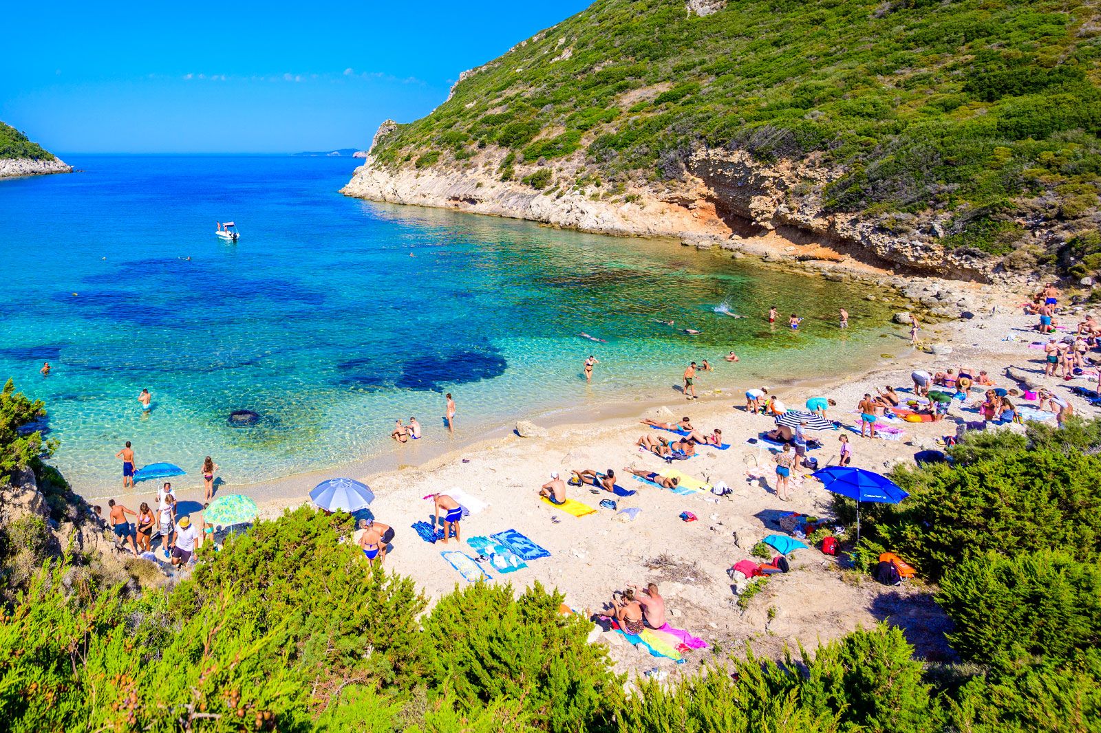 A cove beach with people on the sand with towels and umbrellas