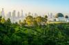 A view of green hilly foliage in front of an observatory and city skyline.