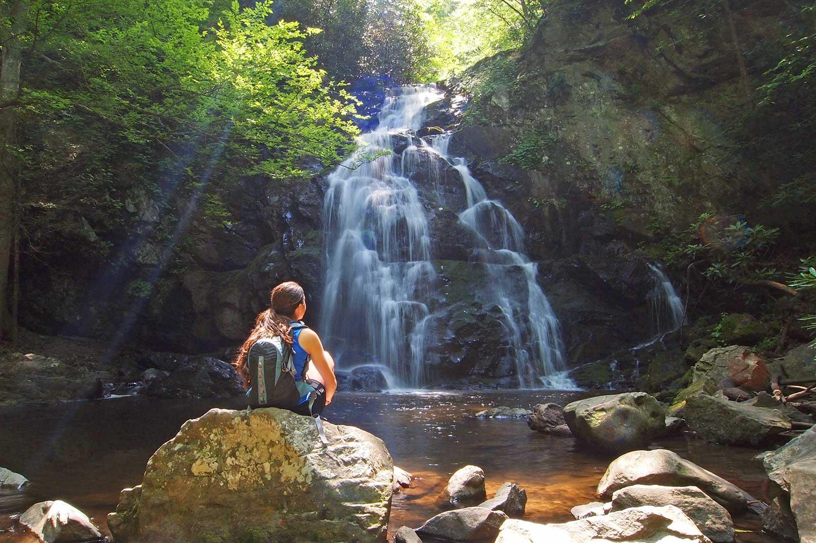 A woman sits in front of a waterfall.