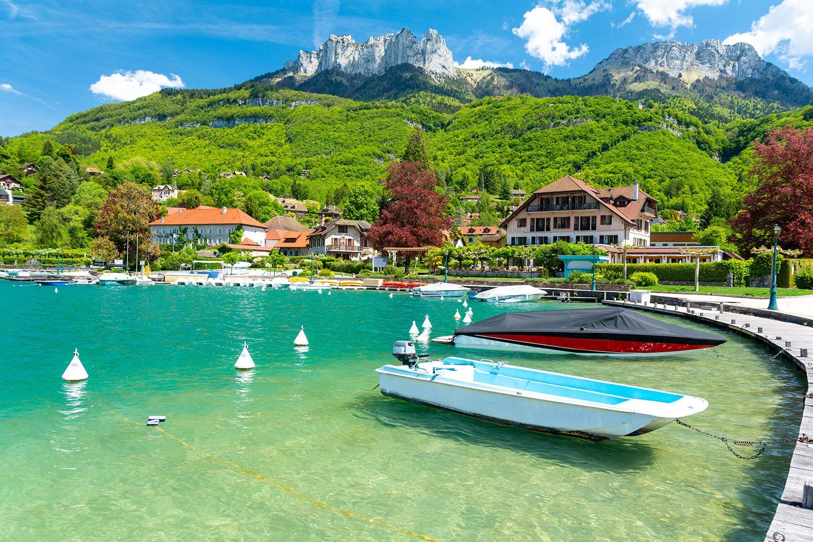 Boats on a clear blue lake with alpine style houses and mountains in the background.