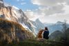 A dog with its owner sitting on the ground, mountains in the background.