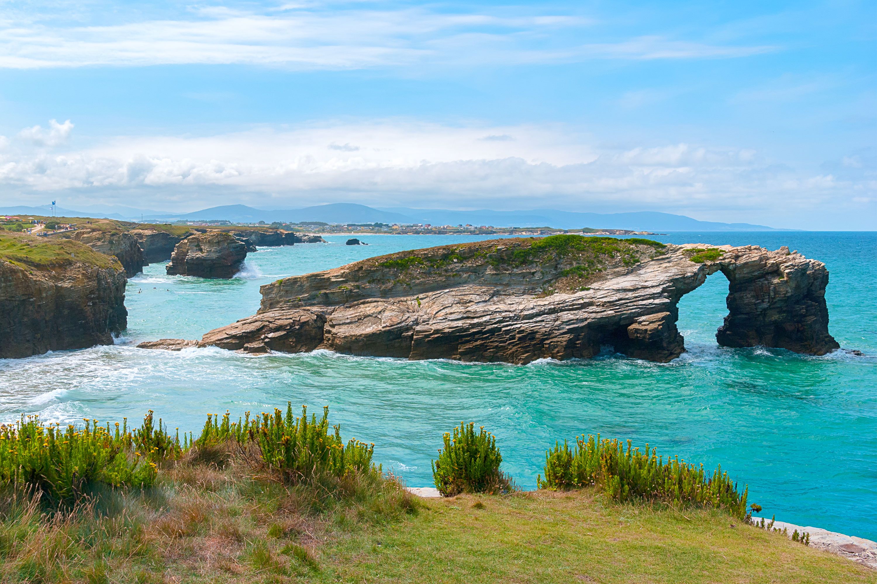 An archway in the rock in the ocean off a coastline.