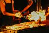 A chef torching meat on a grill in the night.
