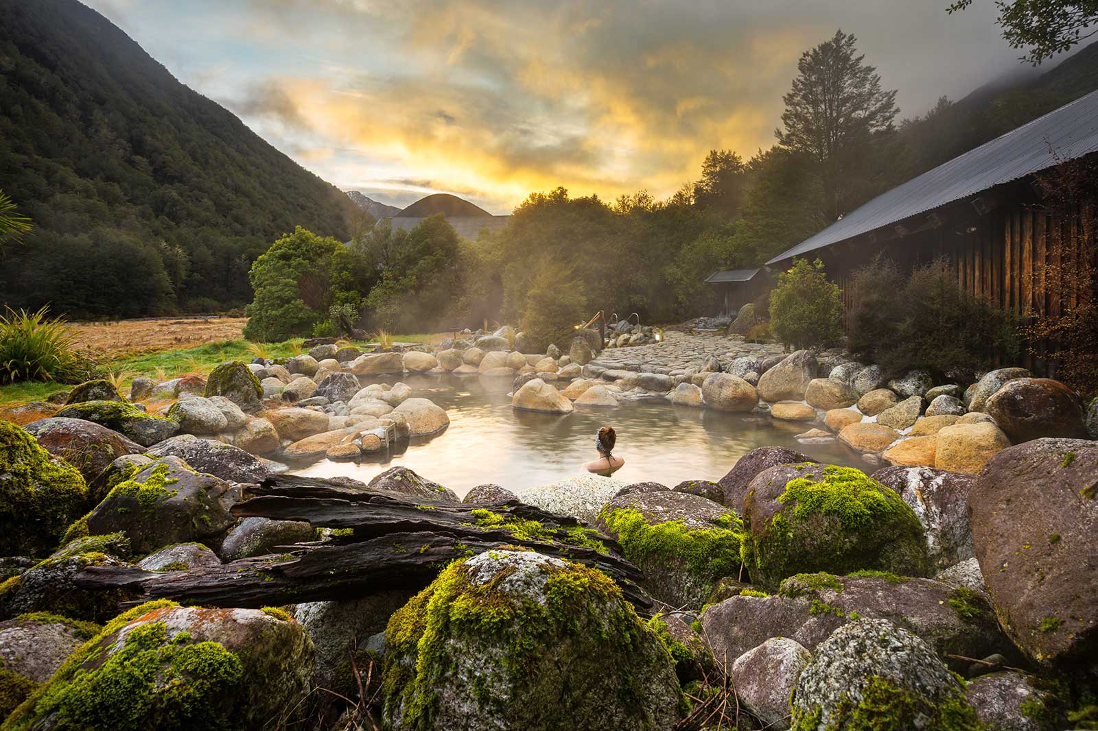 Person in an onsen surrounded by trees and rocks.