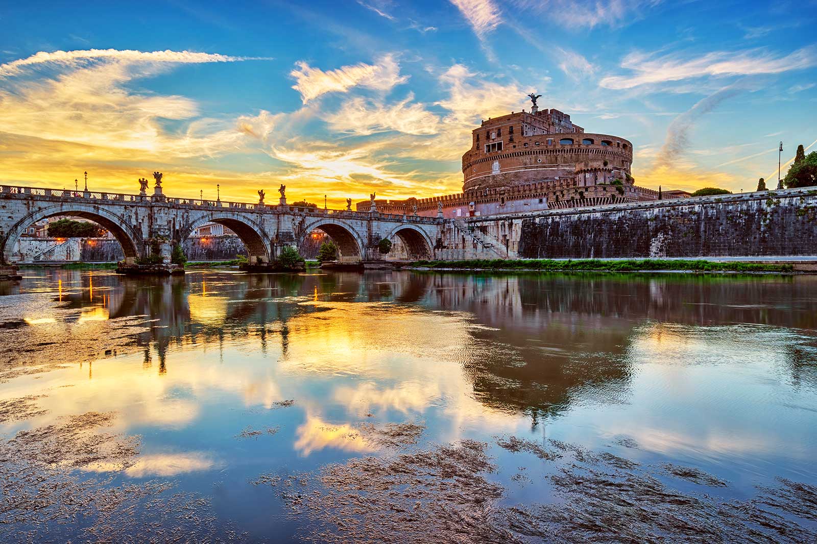 Bridge over a river with a Roman ruin behind it.