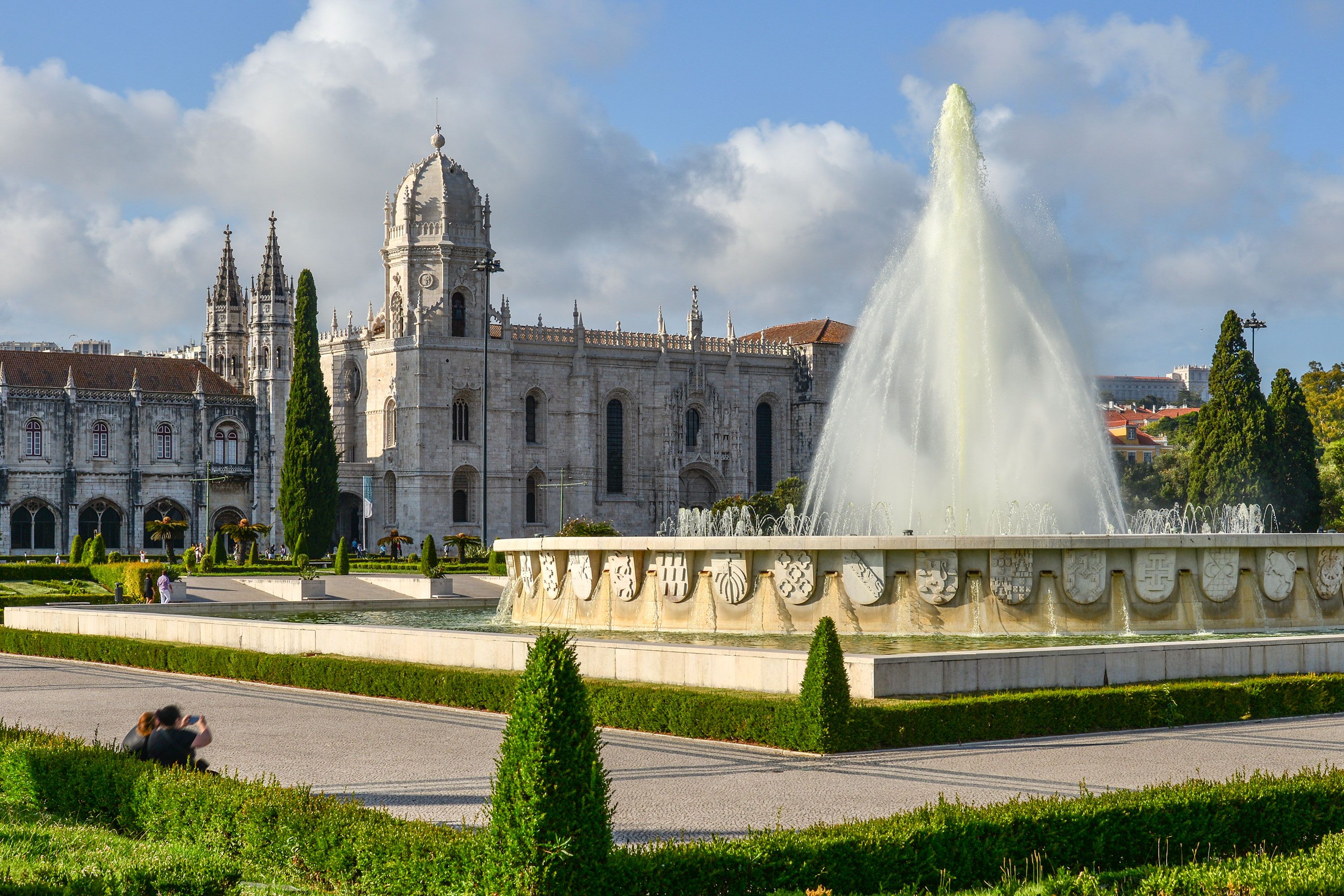 A fountain in a square garden with a large old building in the background.
