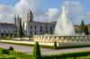 A fountain in a square garden with a large old building in the background.