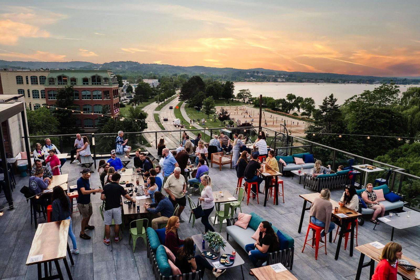People on a rooftop bar with a view of a river.