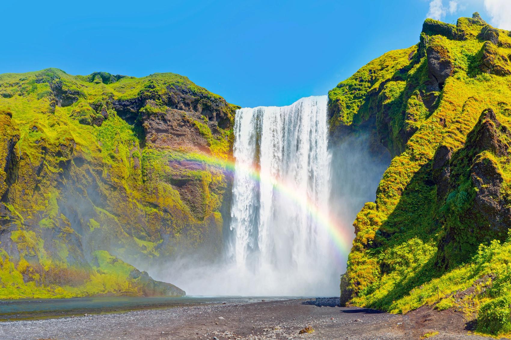 A rainbow crosses through a lush waterfall.