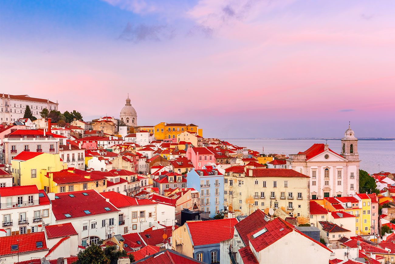A view of a city with red roofs along a coastline at sunset.