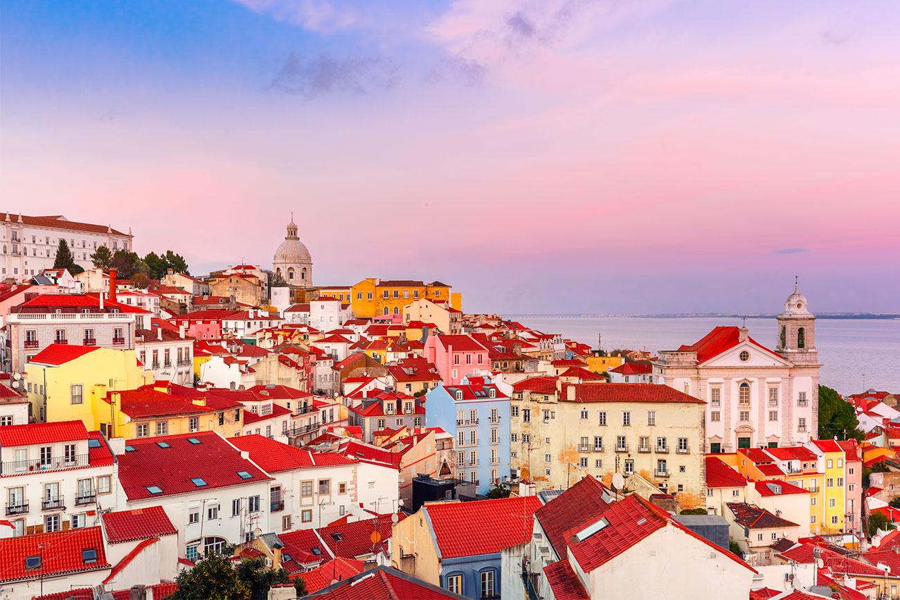 A view of a city with red roofs along a coastline at sunset.