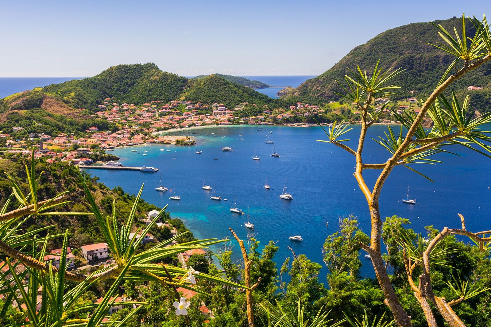 A small town by a blue lagoon surrounded by lush green hills.