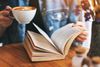 A person holding a cup of coffee and reading a book.