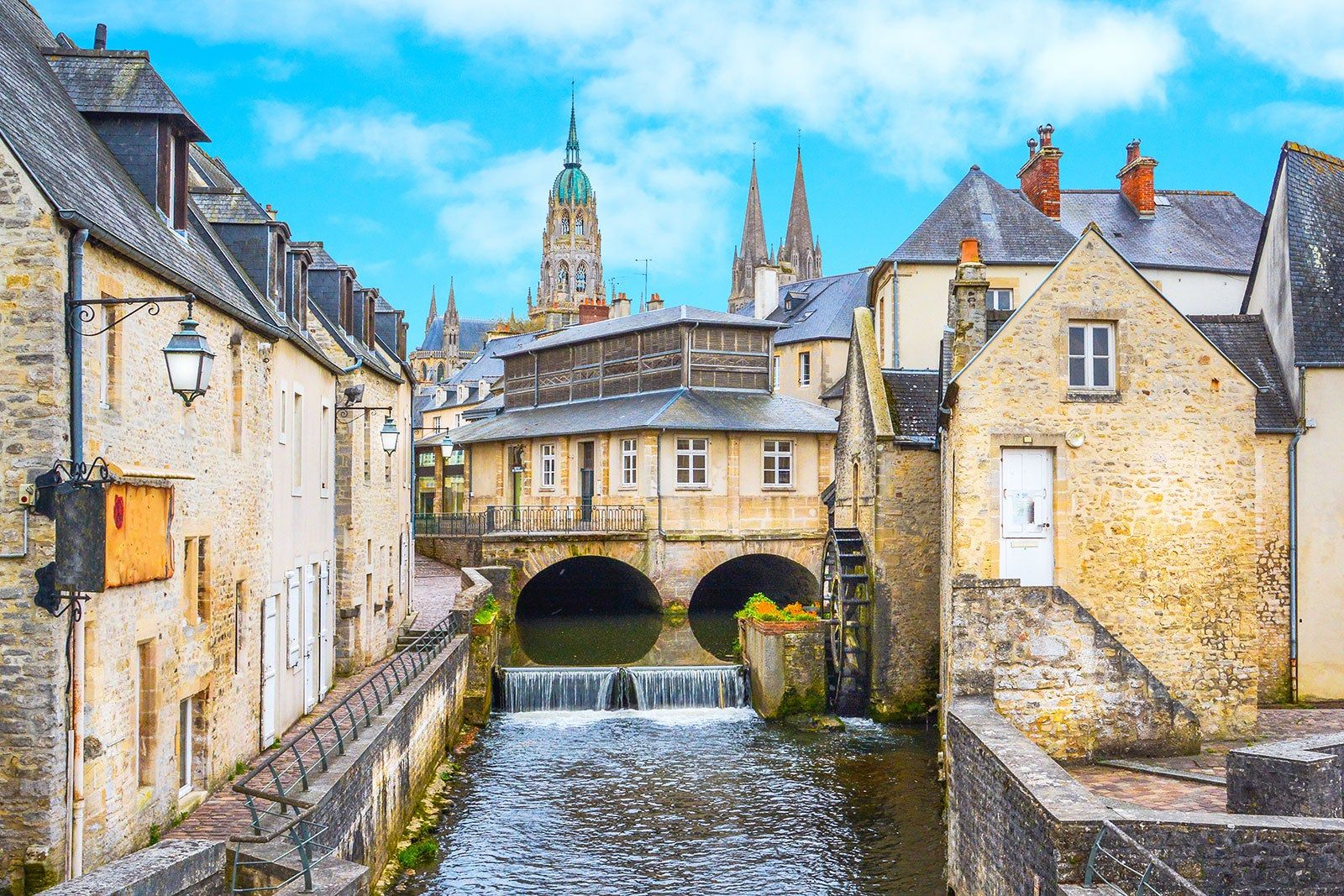 A rustic cityscape with a small waterfall and church spires in the background.