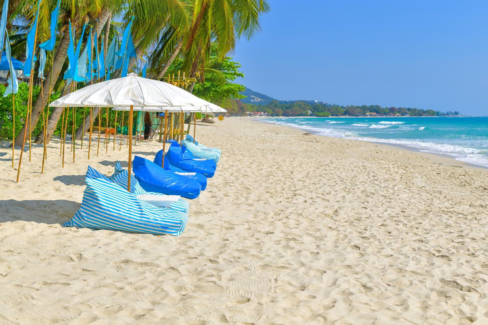 A beach with umbrellas and bean bags.