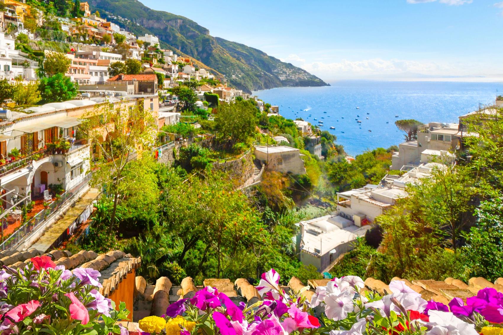 A mountain, city, and sea view through an open window with shutters.