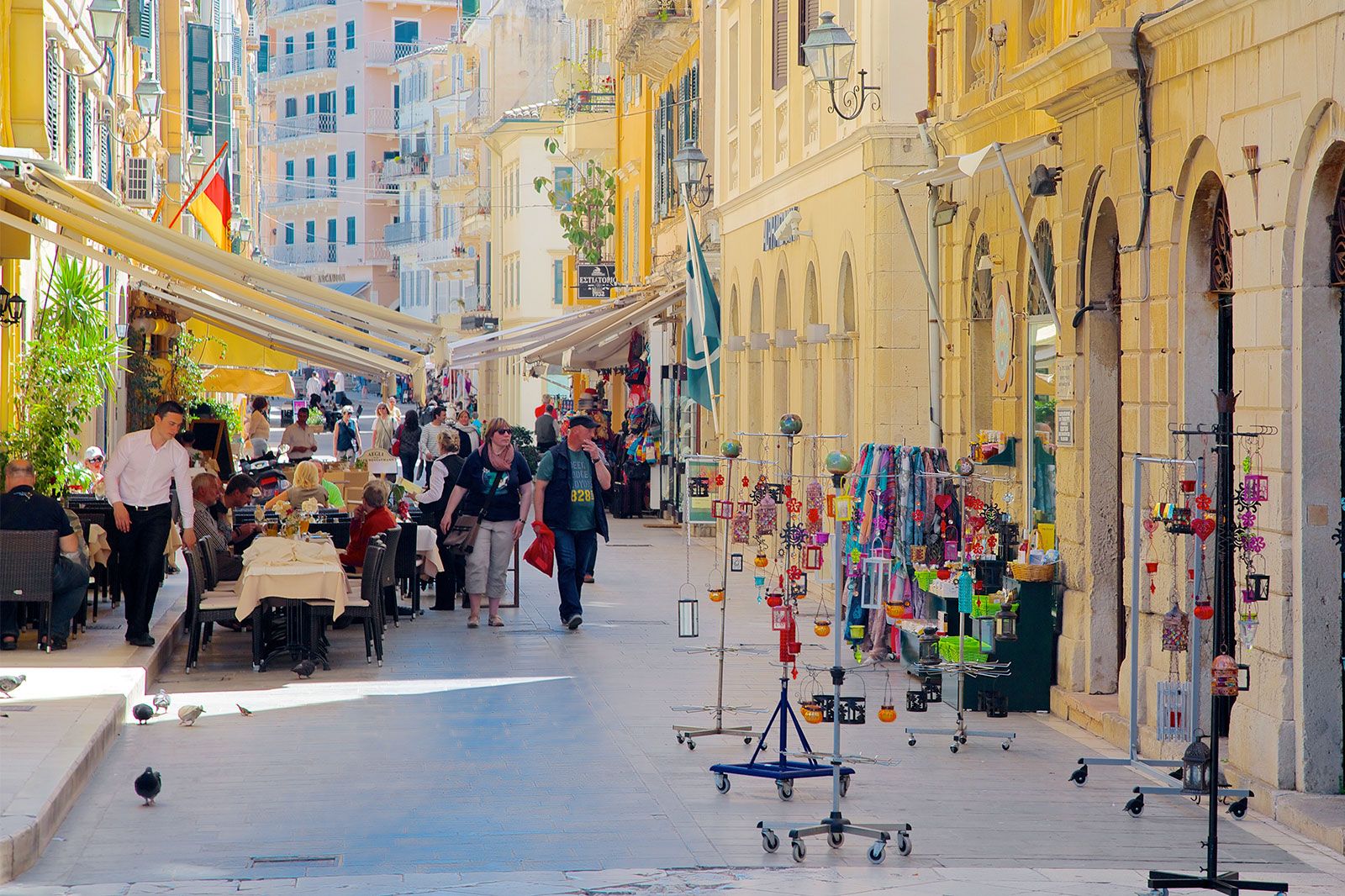People shop and walk down a street with a restaurant. 