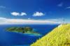 View of a woman standing on a rock surrounded by bright lime green grass looking out over the ocean and an island in the distance in Fiji.