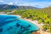A aerial view of a blue water cove and sandy beach with green jungle.