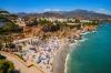 A view from above of Calahonda Beach and its brightly colored parasols and cliffs and broken rocks with whitewashed buildings and mountains in the distance in Nerja, Andalusia.