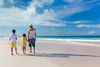 Father and kids standing on the white sands of a beach and the ocean in the background.
