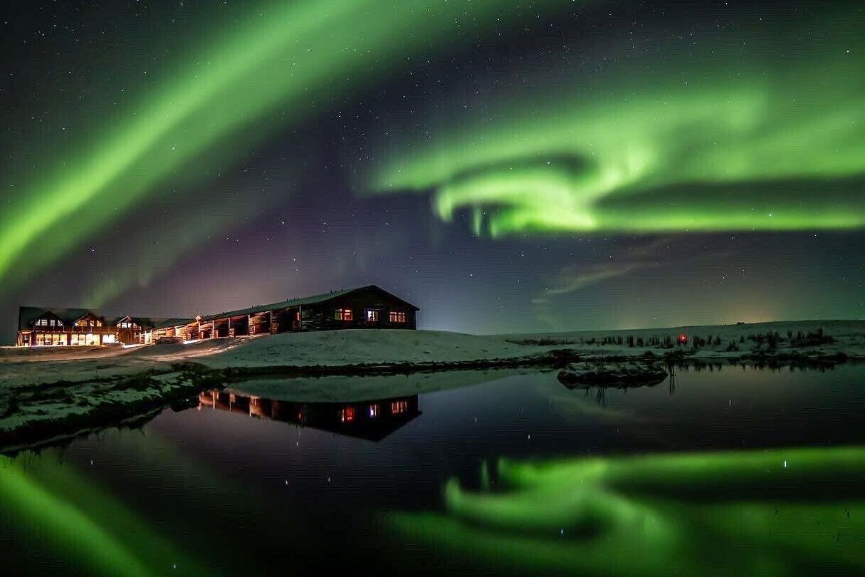 The Aurora borealis over a hotel and lake at night time.