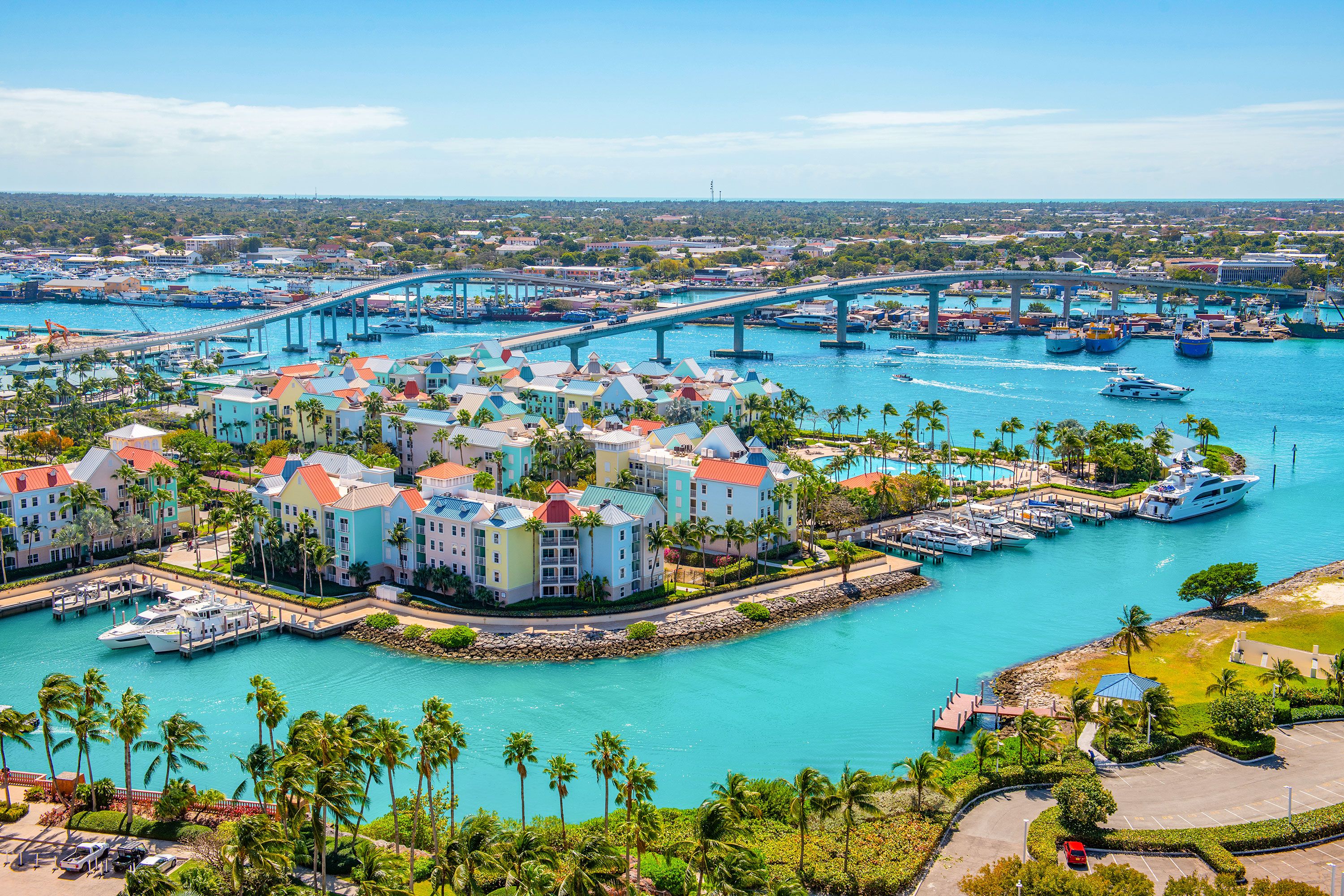 Aerial view of harbor with multistory residential buildings, palm trees, tankers, bridges and blue water.