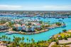 Aerial view of harbor with multistory residential buildings, palm trees, tankers, bridges and blue water.