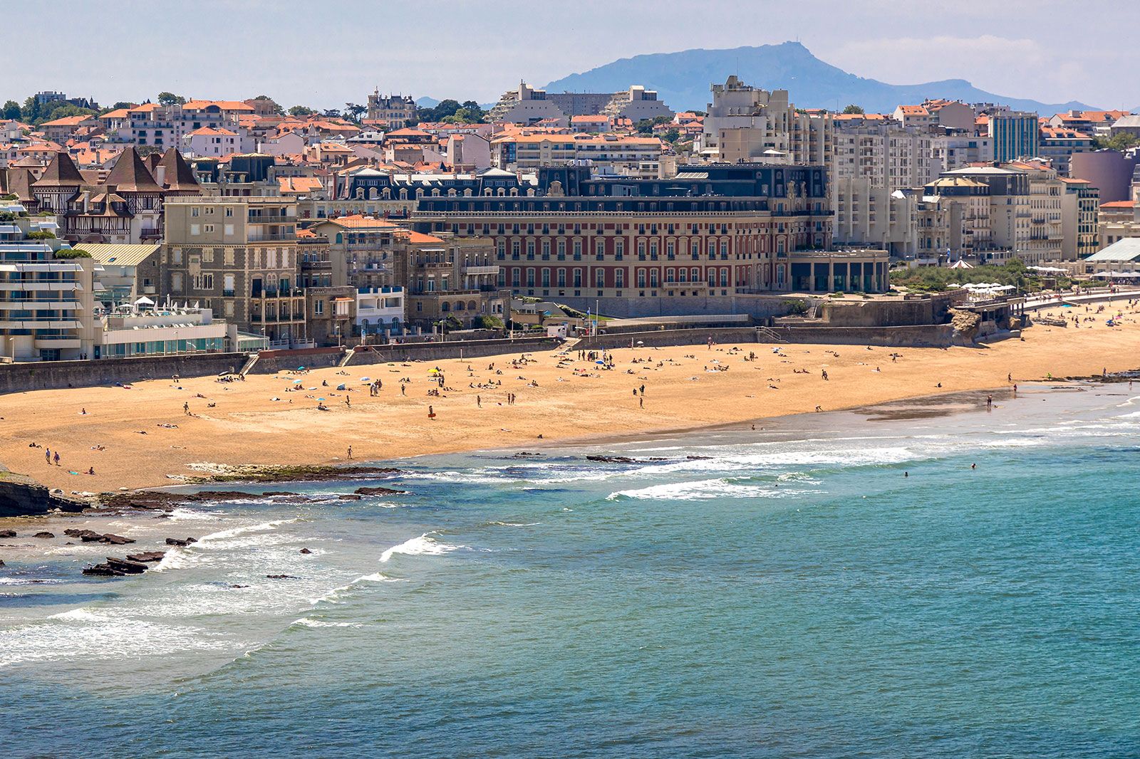 A blue beach with crowd of people enjoying with town in the background.
