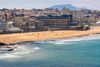 A blue beach with crowd of people enjoying with town in the background.