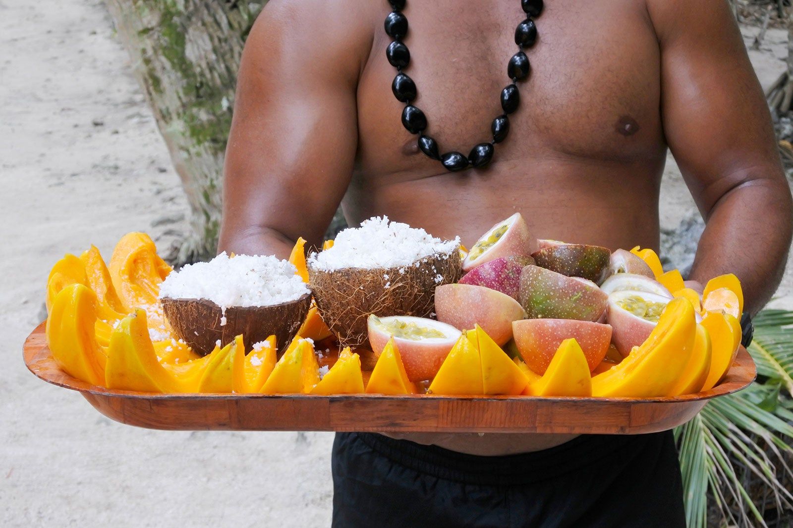 Man holds a tray with Fijian foods and fruits.