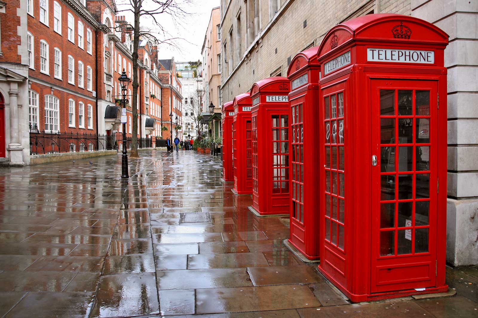 Five red telephone boxes in a street corner.
