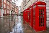 Five red telephone boxes in a street corner.